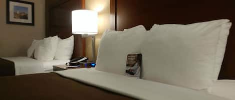 Une chambre d’hôtel avec un lit, des oreillers, une lampe de chevet, un téléphone et un tableau encadré au mur.