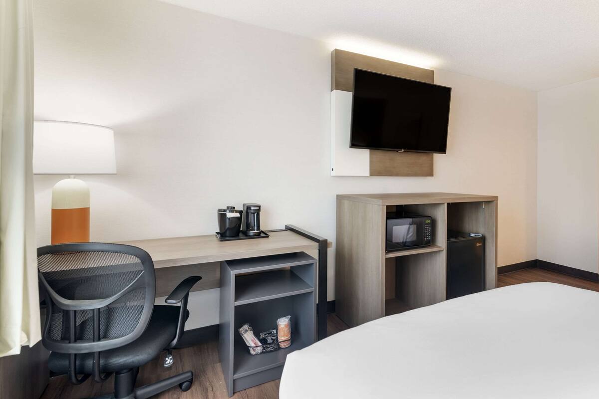 A hotel room with a bed, a desk with a chair, a television mounted on the wall, a microwave, and a coffee maker.