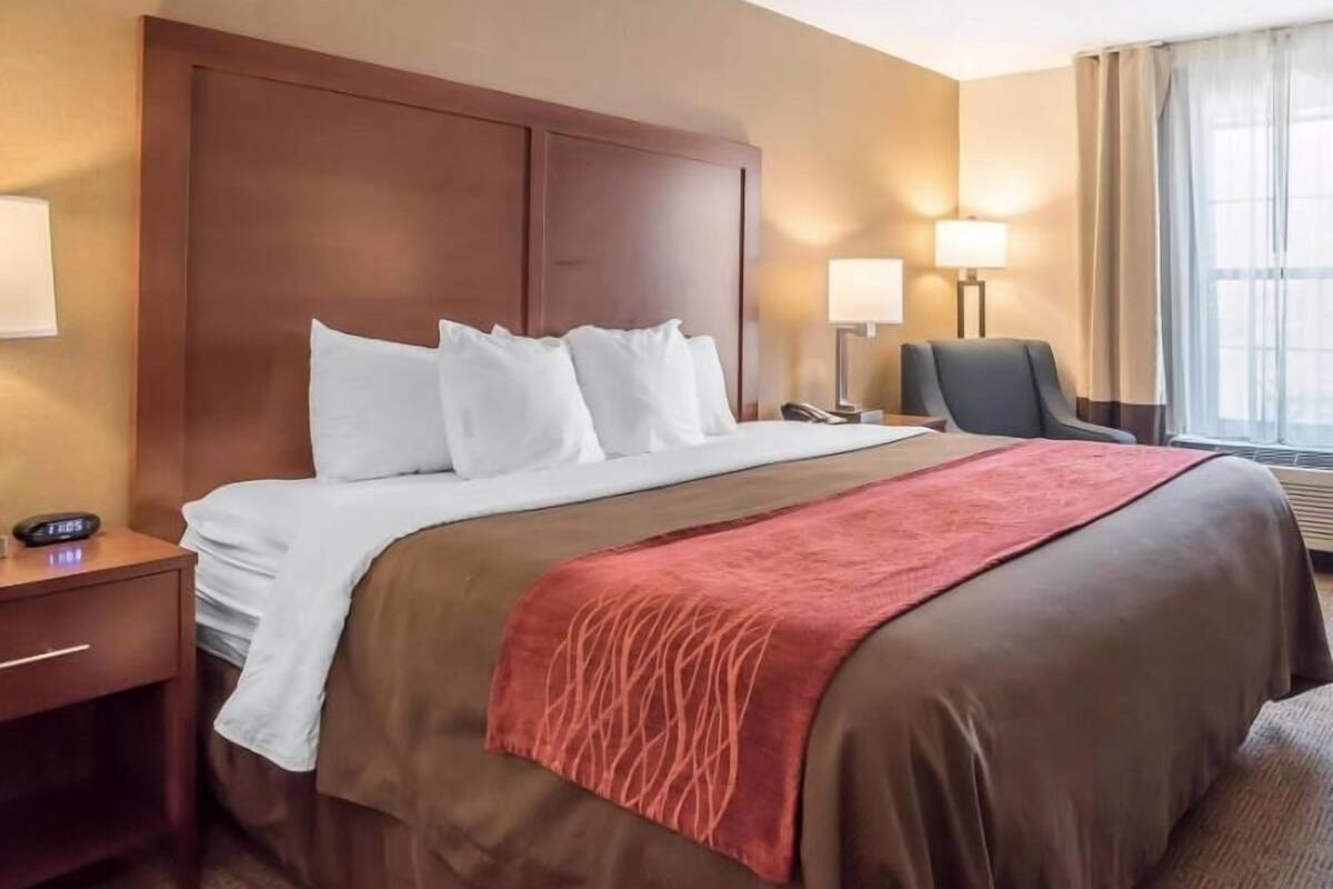 A hotel room with a bed, bedside tables, lamps, a chair, and a window with curtains.