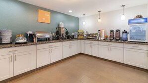 A modern kitchen with white cabinets, a granite countertop, and various appliances including a coffee maker, waffle maker, and hot water dispenser.