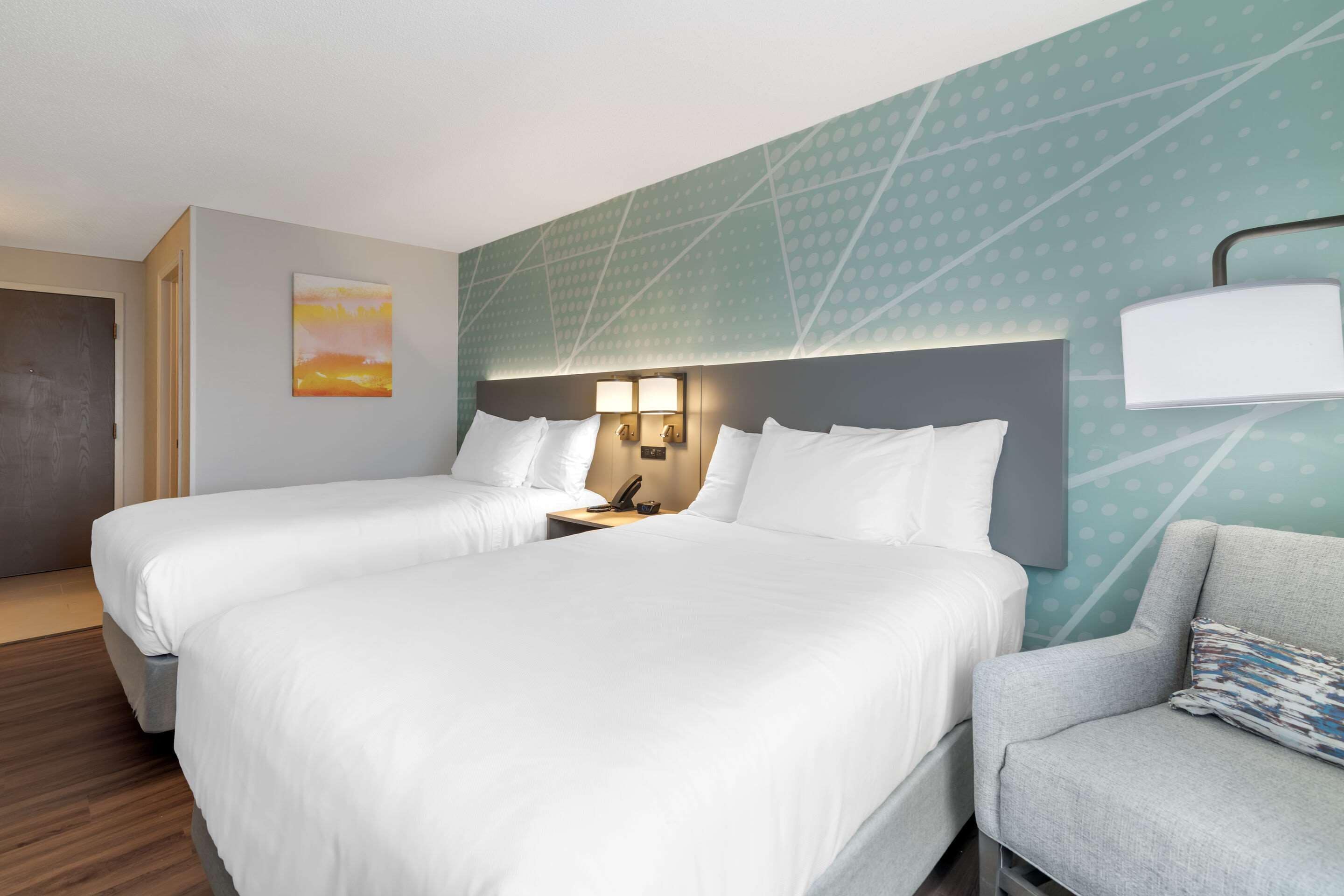 Ein Hotelzimmer mit zwei Betten, einem Schlafsofa, einem Nachttisch mit Lampe und einer Wand mit geometrischem Muster.