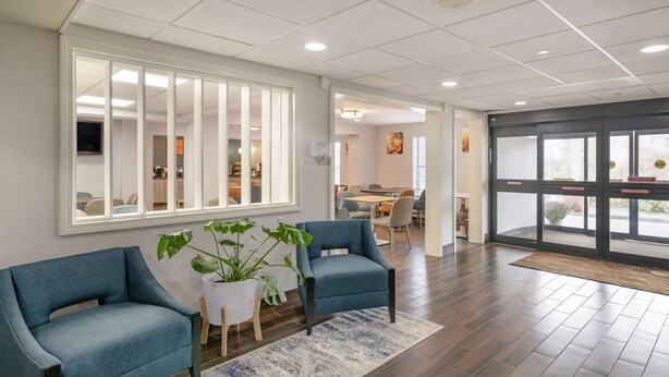 A spacious living area with two blue armchairs, a small white table, and a large window with blinds.