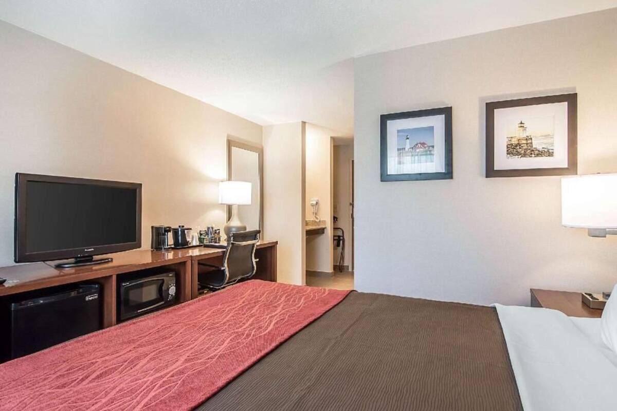 A hotel room with a bed, a TV, a desk with a lamp, a microwave, and framed pictures on the wall.