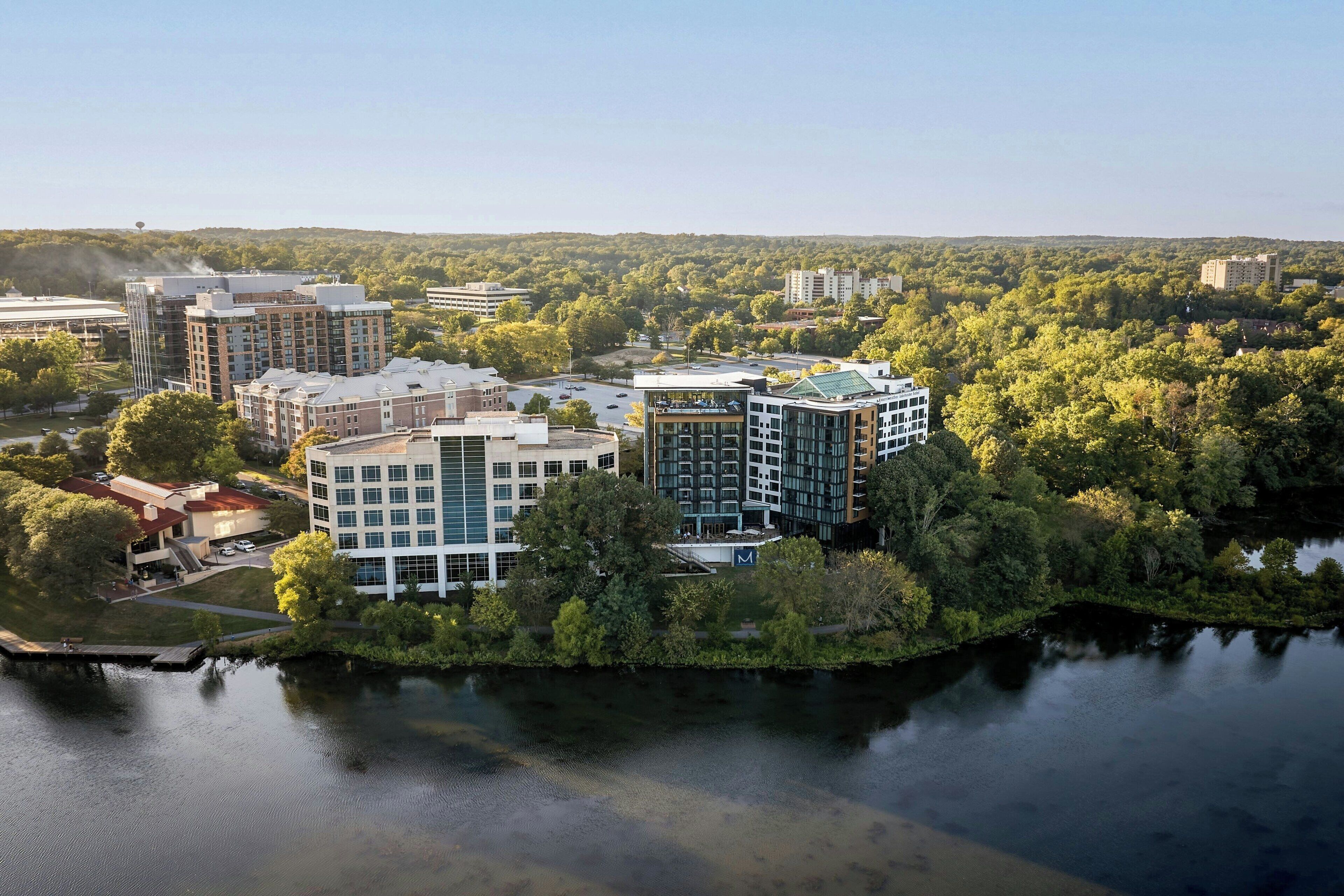 Un moderno complejo hotelero con varias edificaciones, un río al frente y vegetación circundante.