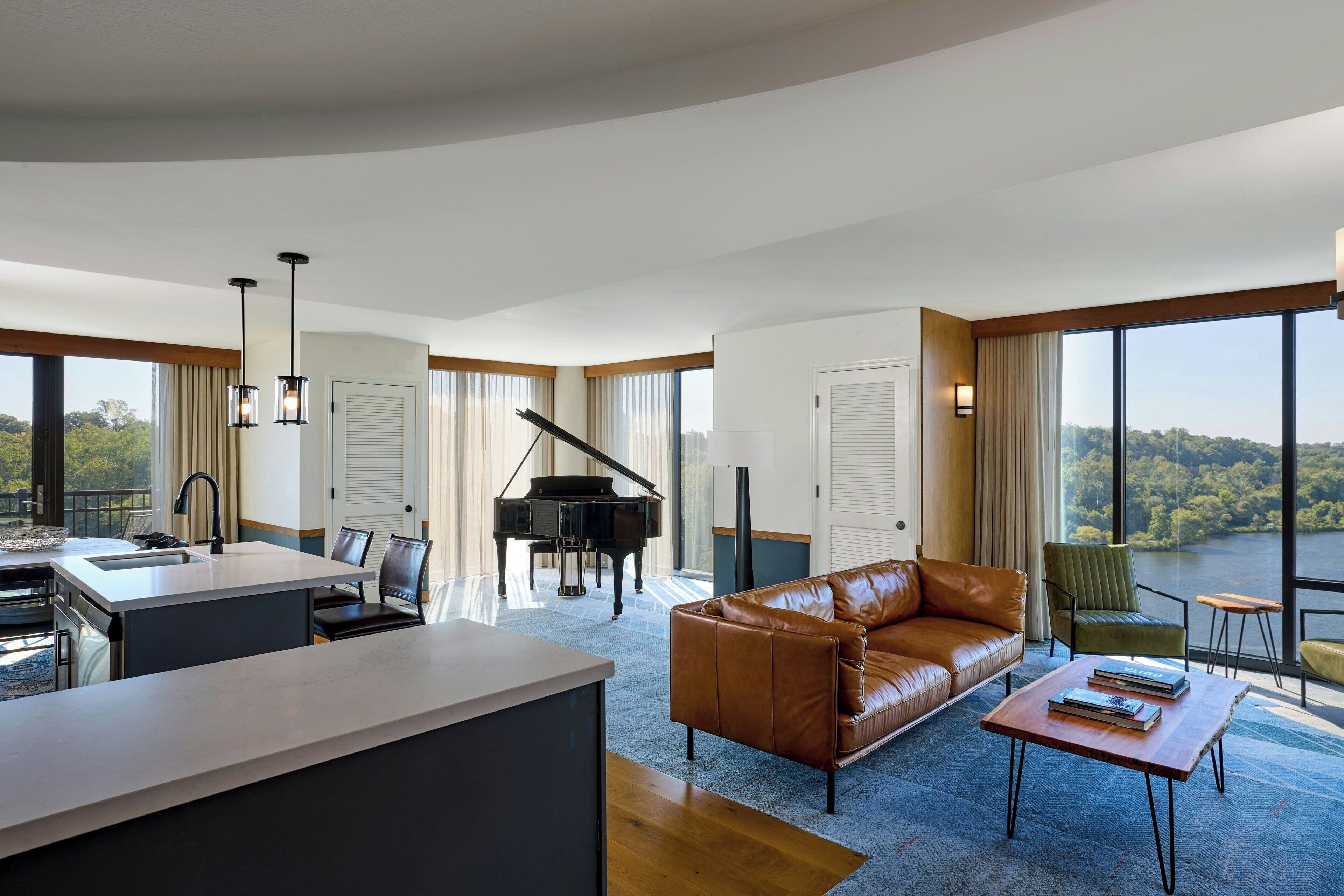 Un vaste espace de vie comprenant un piano, un canapé en cuir et donnant sur un lac.
