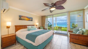 Een slaapkamer met een groot bed, een plafondventilator, een schilderij, een balkon met uitzicht op de oceaan en een zithoek met uitzicht.