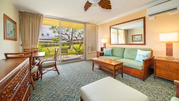 Ein Hotelzimmer mit einer großen Schiebetür zu einem Balkon, einem Sofa, einem Couchtisch, einem Schreibtisch mit Schubladen und einem Spiegel an der Wand.