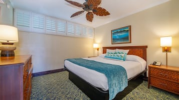 A hotel room with a bed, a ceiling fan, a nightstand, a lamp, and a painting on the wall.