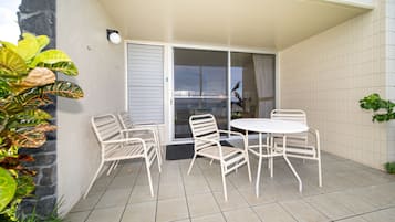 Une terrasse avec une table et des chaises blanches, une porte-fenêtre coulissante et des plantes en pot.
