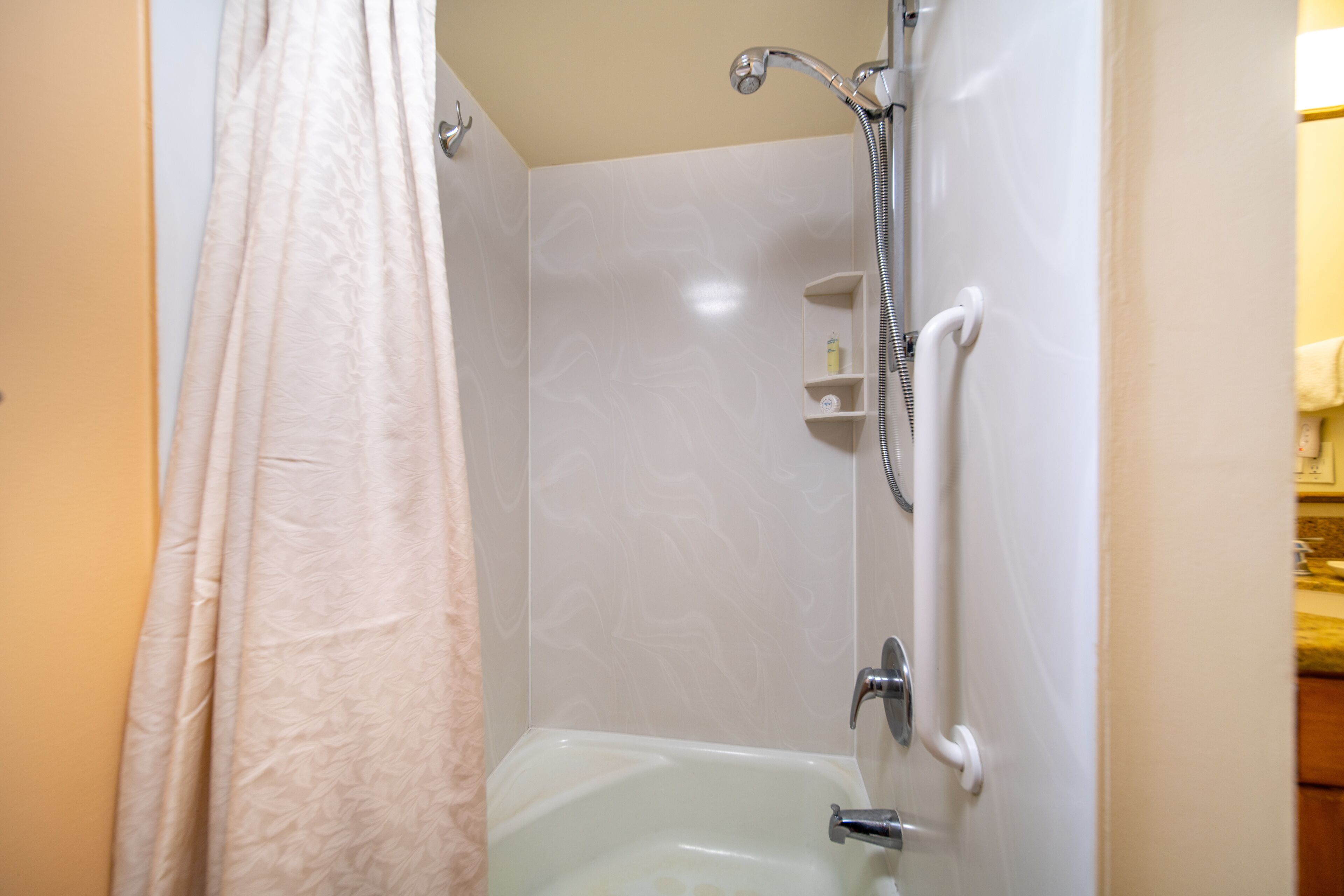 A bathroom with a shower, a bathtub, and a handrail.