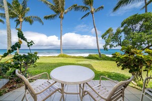 Un patio con una mesa redonda y dos sillas, con vistas a una playa con palmeras y el océano.