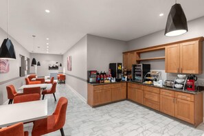 A modern kitchen with wooden cabinets, a coffee station, and orange chairs. - Days Inn by Wyndham Kenner/New Orleans Airport South (Kenner)
