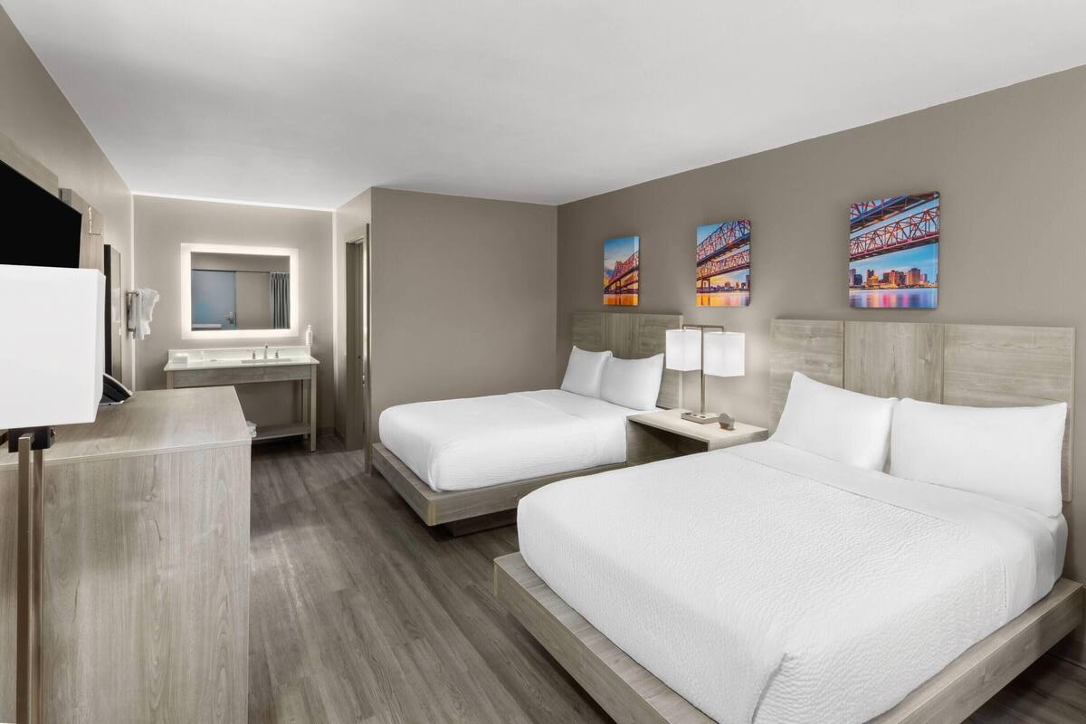 A hotel room with two beds, a desk, a mirror, and artwork on the wall.