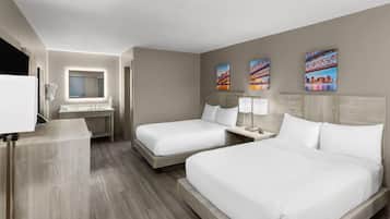 A hotel room with two beds, a desk, a mirror, and artwork on the wall.