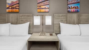 A hotel room with two beds, a nightstand with a lamp, and three paintings of a bridge on the wall.
