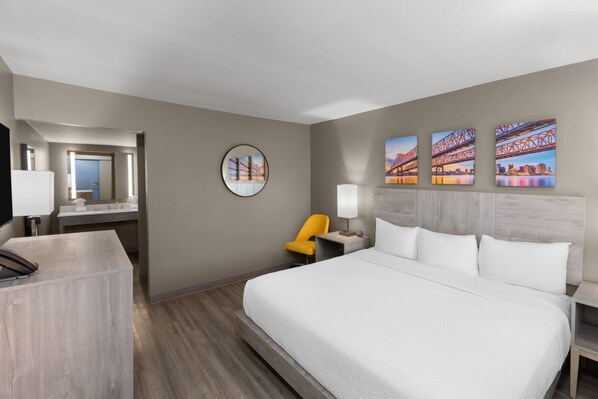 A hotel room with a large bed, a desk, a chair, a round mirror, and three paintings on the wall. - Days Inn by Wyndham Kenner/New Orleans Airport South (Kenner)