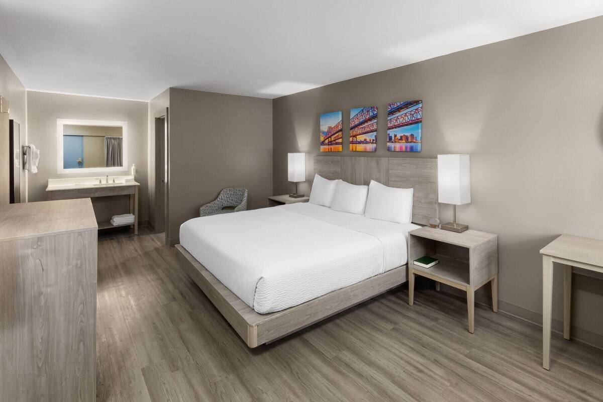A modern hotel room with a large bed, a vanity with a mirror, and artwork on the wall.