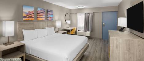 Habitación de hotel con una cama grande, un escritorio, una silla, un televisor y obras de arte en la pared.