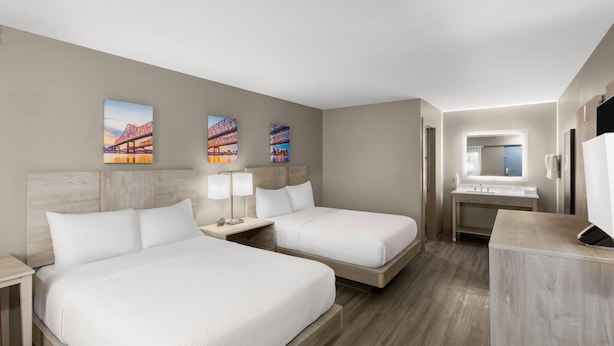 Ein Hotelzimmer mit zwei Betten, einem Badezimmer mit Waschbecken und Spiegel sowie einem Bild an der Wand.
