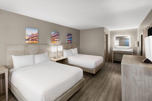 A hotel room with two beds, a bathroom with a sink and mirror, and artwork on the wall. - Days Inn by Wyndham Kenner/New Orleans Airport South (Kenner)