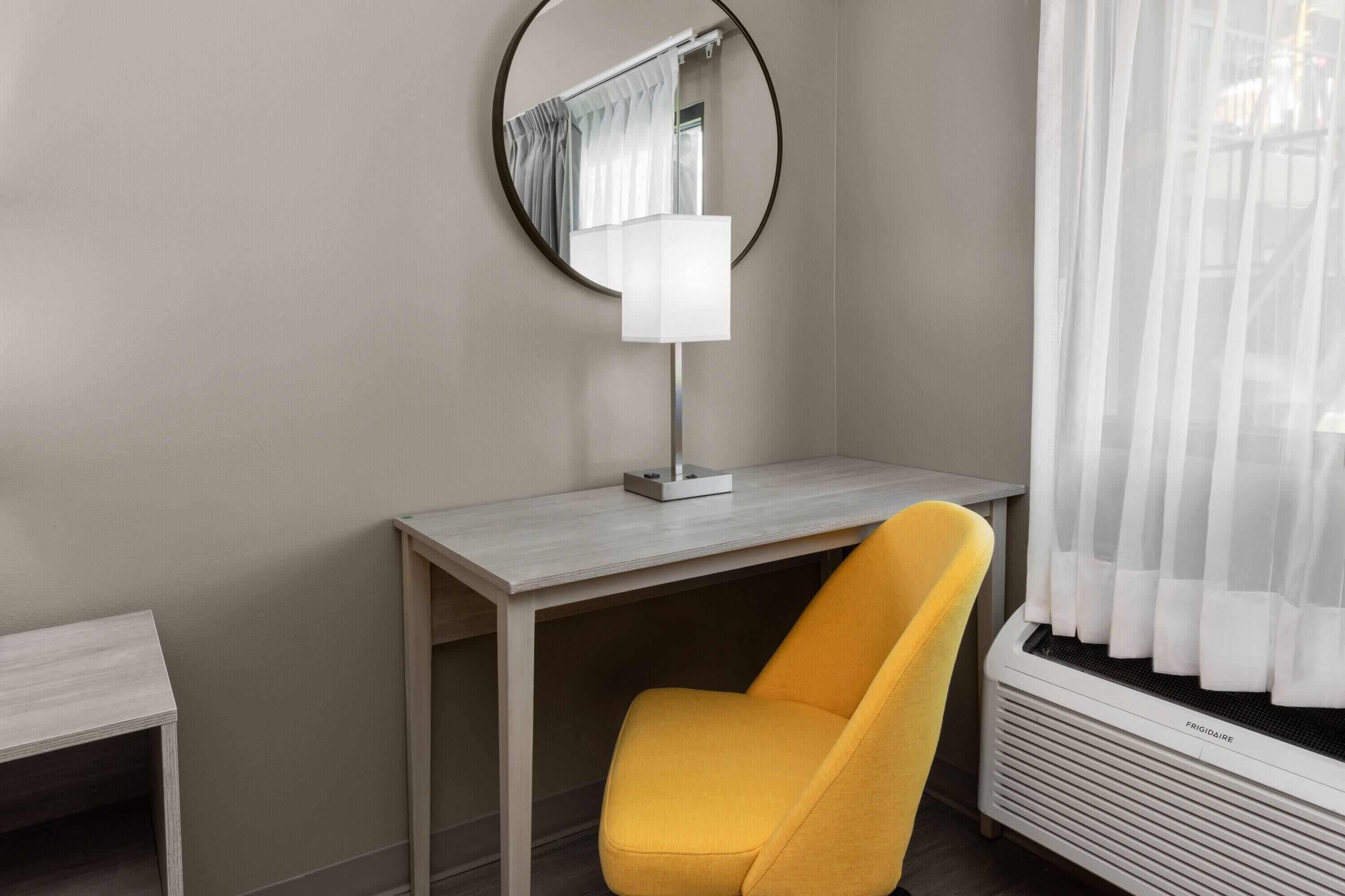 A room with a desk, a chair, a mirror, and a window with curtains.