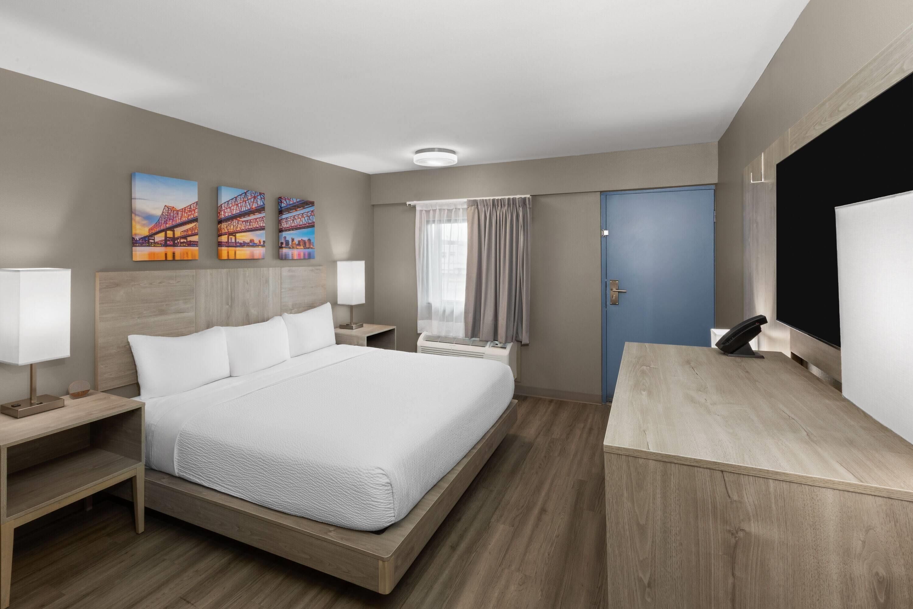 A hotel room with a large bed, bedside tables, a desk, and a window with curtains.