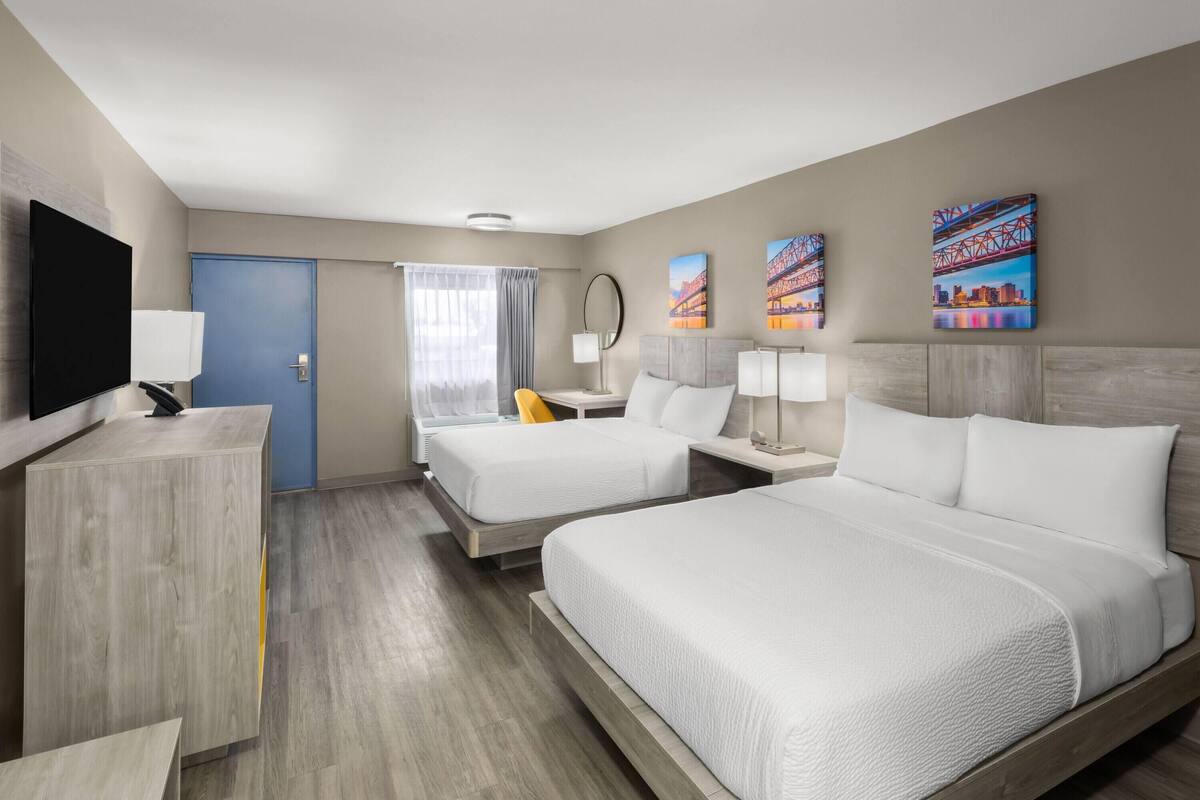 A hotel room with two beds, a desk, a TV, and artwork on the walls.