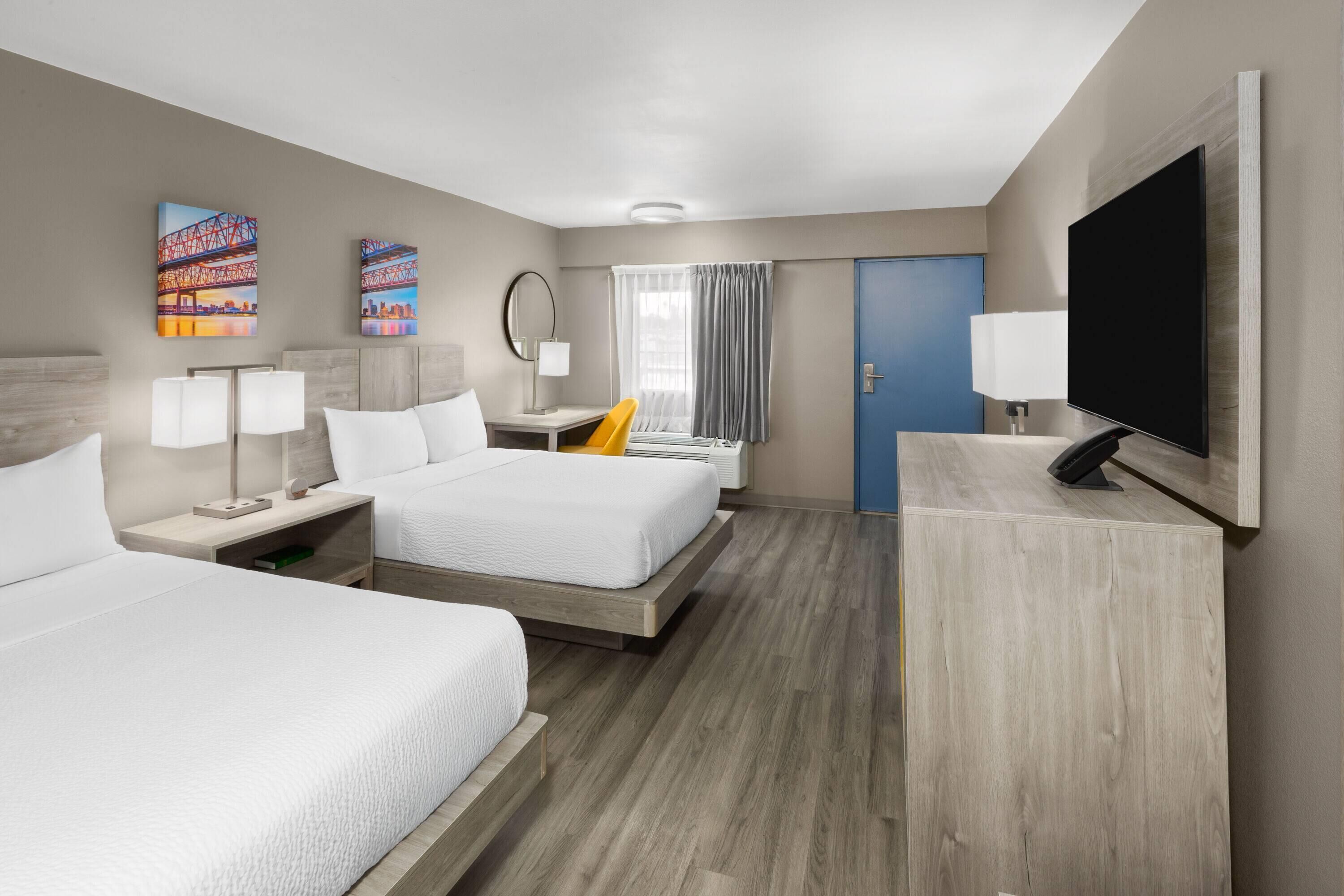 A hotel room with two beds, a desk, a TV, and artwork on the walls.