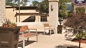 An outdoor seating area with benches and planters, a Hampton Inn sign, and a building in the background. - Hampton Inn Atlanta Buckhead (Atlanta)