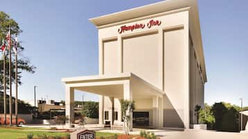 A modern Hampton Inn with a prominent entrance, a covered outdoor seating area, and a landscaped garden.