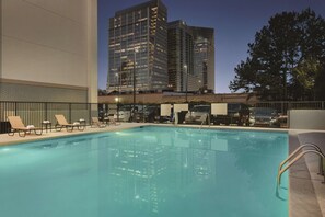 A swimming pool with lounge chairs and a view of tall buildings at dusk.