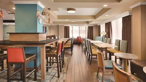 A hotel dining area with multiple tables and chairs, a central bar, and a view of the city through large windows. - Hampton Inn Atlanta Buckhead (Atlanta)
