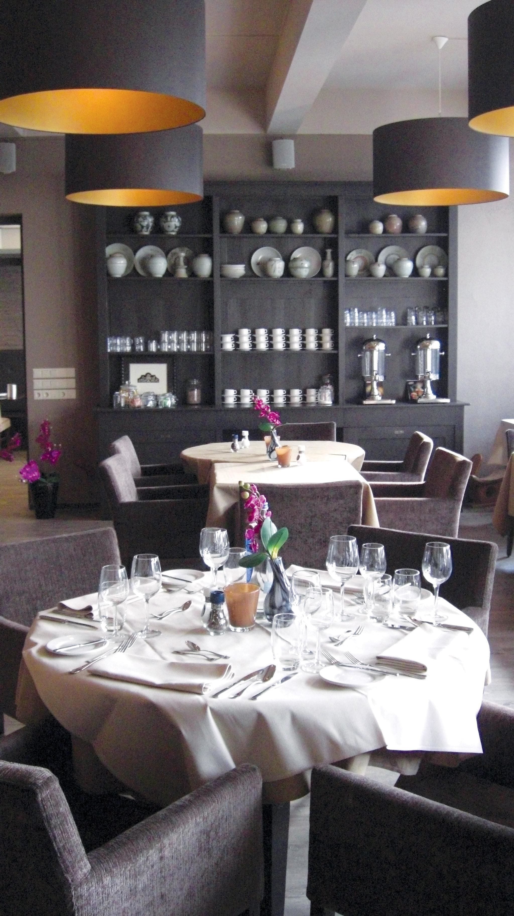 Un restaurante con mesas redondas dispuestas para comer, con mantel blanco, cubiertos y copas de vino.