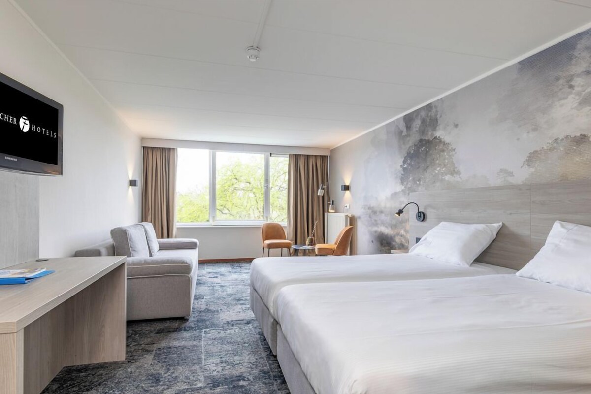 Ein Hotelzimmer mit einem großen Bett, einem Schreibtisch, einer Couch und einem Fernseher an der Wand.