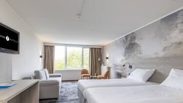 A hotel room with a large bed, a desk, a sofa, and a TV mounted on the wall.