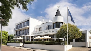 Et moderne hotel med et markant tårn, udendørs siddepladser og en klar himmel.