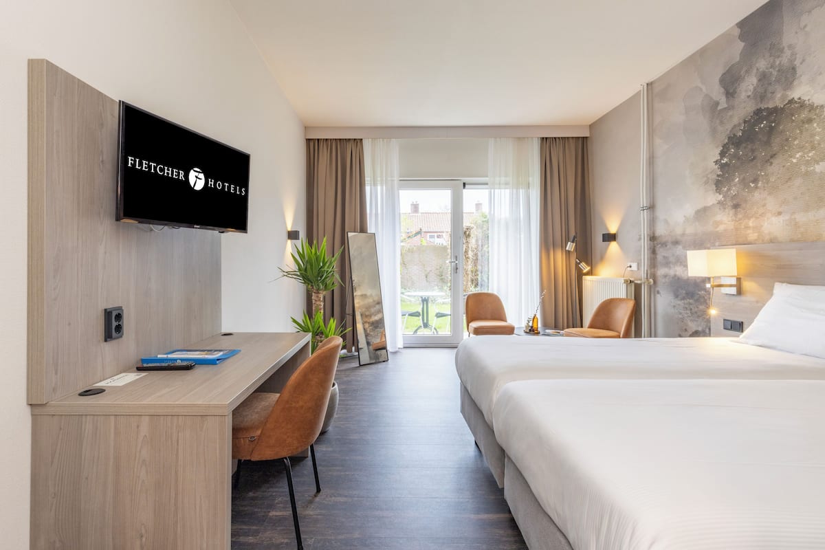 Ein Hotelzimmer mit Bett, Schreibtisch, Stuhl, Fernseher und Blick ins Freie.
