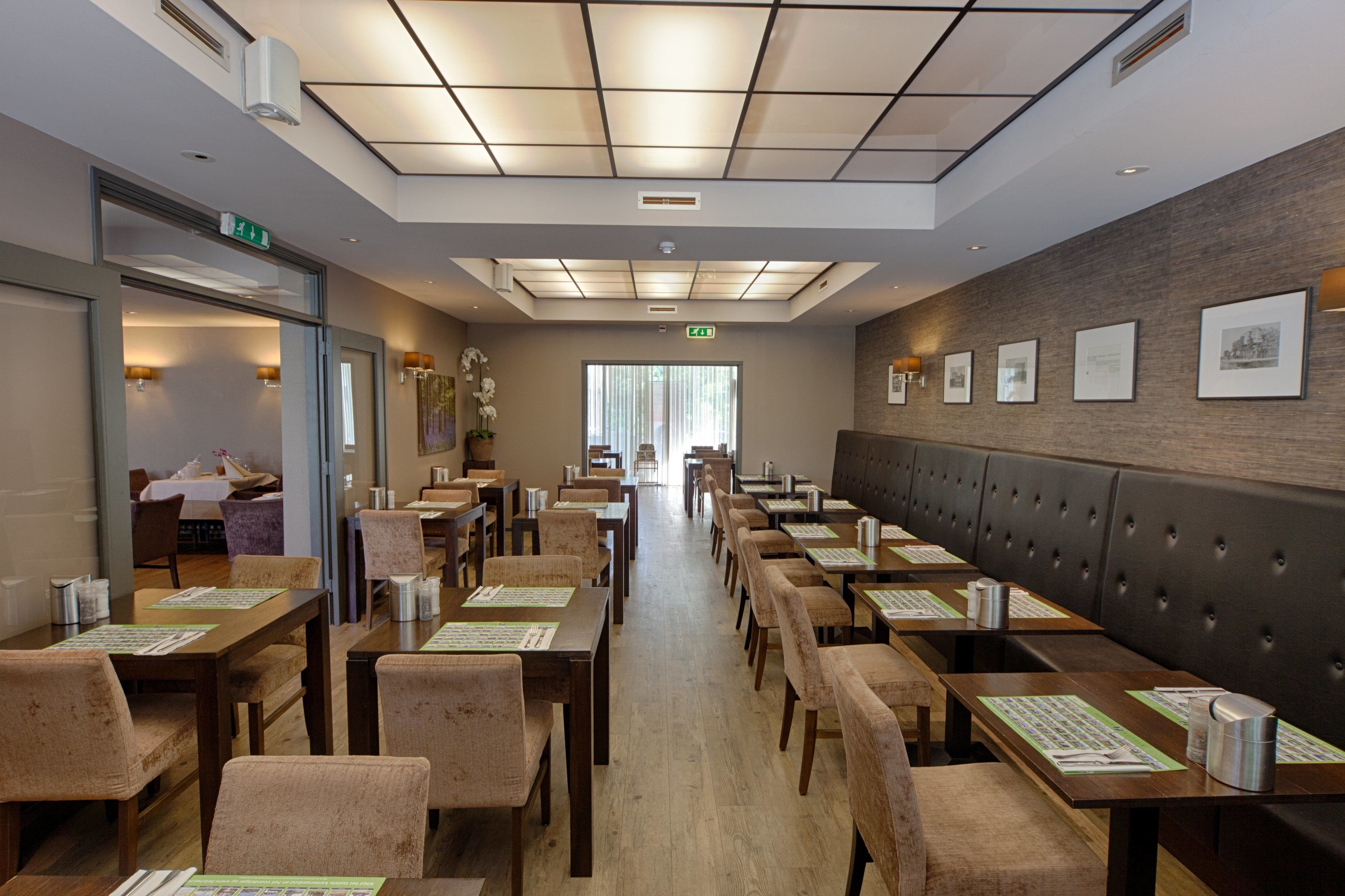 Un restaurante con mesas y sillas de madera, una barra alargada y una pared con cuadros enmarcados.