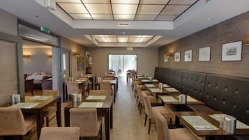 Un restaurante con mesas y sillas de madera, una barra alargada y una pared con cuadros enmarcados.