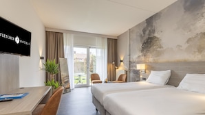 Et hotelværelse med to senge, et skrivebord, stole, et fjernsyn og udsigt til det fri.