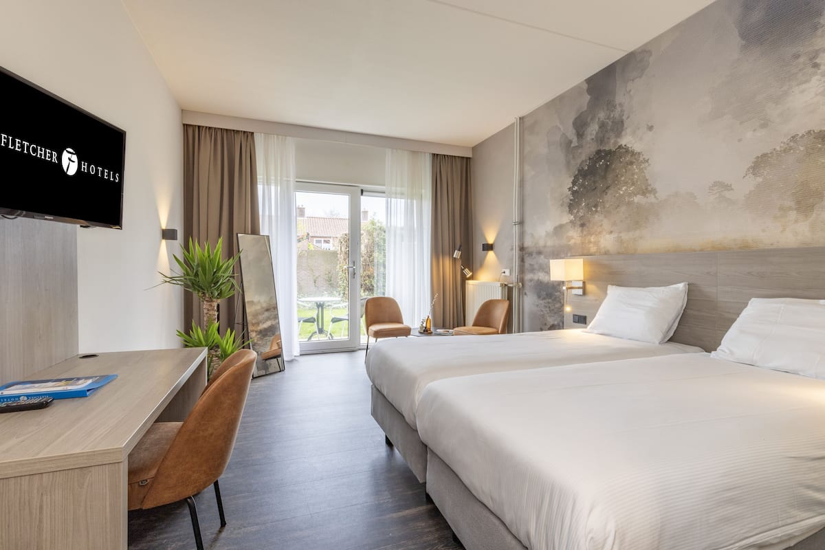 Ein Hotelzimmer mit zwei Betten, einem Schreibtisch, Stühlen, einem Fernseher und Blick ins Freie.