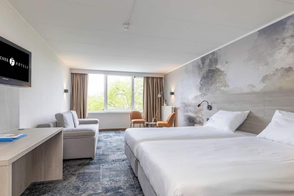 Ein Hotelzimmer mit einem großen Bett, einem Schreibtisch, einer Couch und einem Fernseher an der Wand.