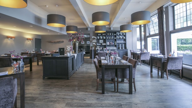 En rummelig restaurant med høje lofter, hængende lamper og et centralt barområde.
