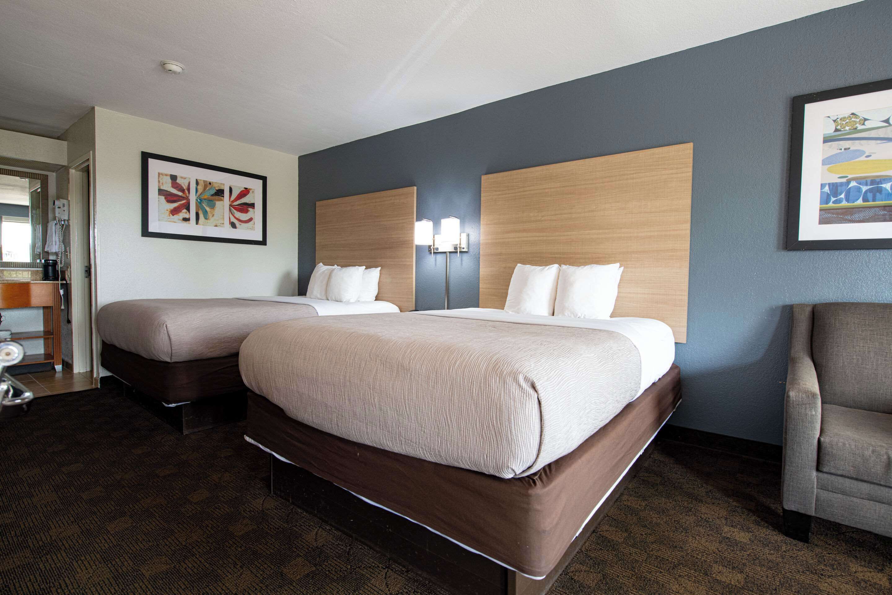 Una habitación de hotel con dos camas, un escritorio con una silla y obras de arte en las paredes.