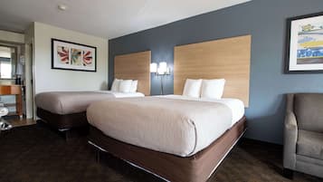 A hotel room with two beds, a desk with a chair, and artwork on the walls.
