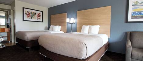 A hotel room with two beds, a desk with a chair, and artwork on the walls.