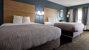 A hotel room with two beds, dark blue walls, and a large window with curtains.