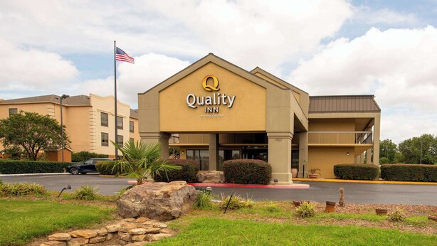 A Quality Inn by Choice Hotels building with a prominent American flag, a parking lot, and landscaped surroundings.