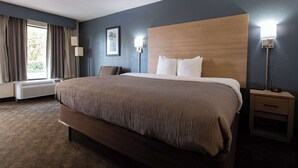 Una habitación de hotel con una cama grande, una mesita de noche con lámpara, una ventana con cortinas y un aire acondicionado instalado en la pared.