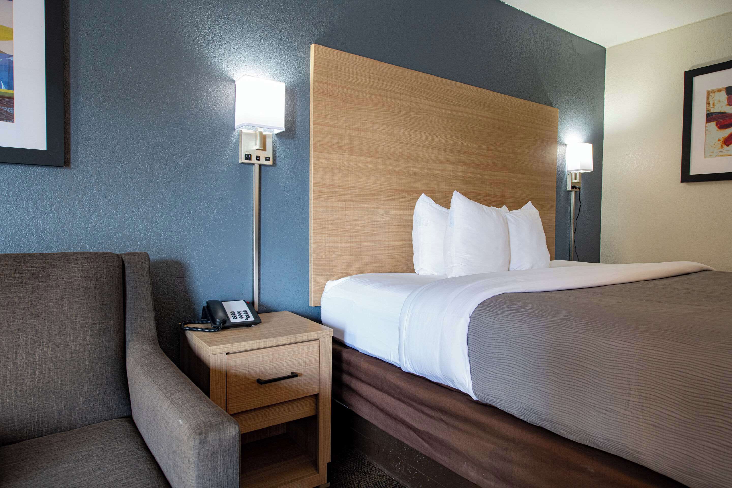 A hotel room with a bed, a nightstand with a phone, and a chair.